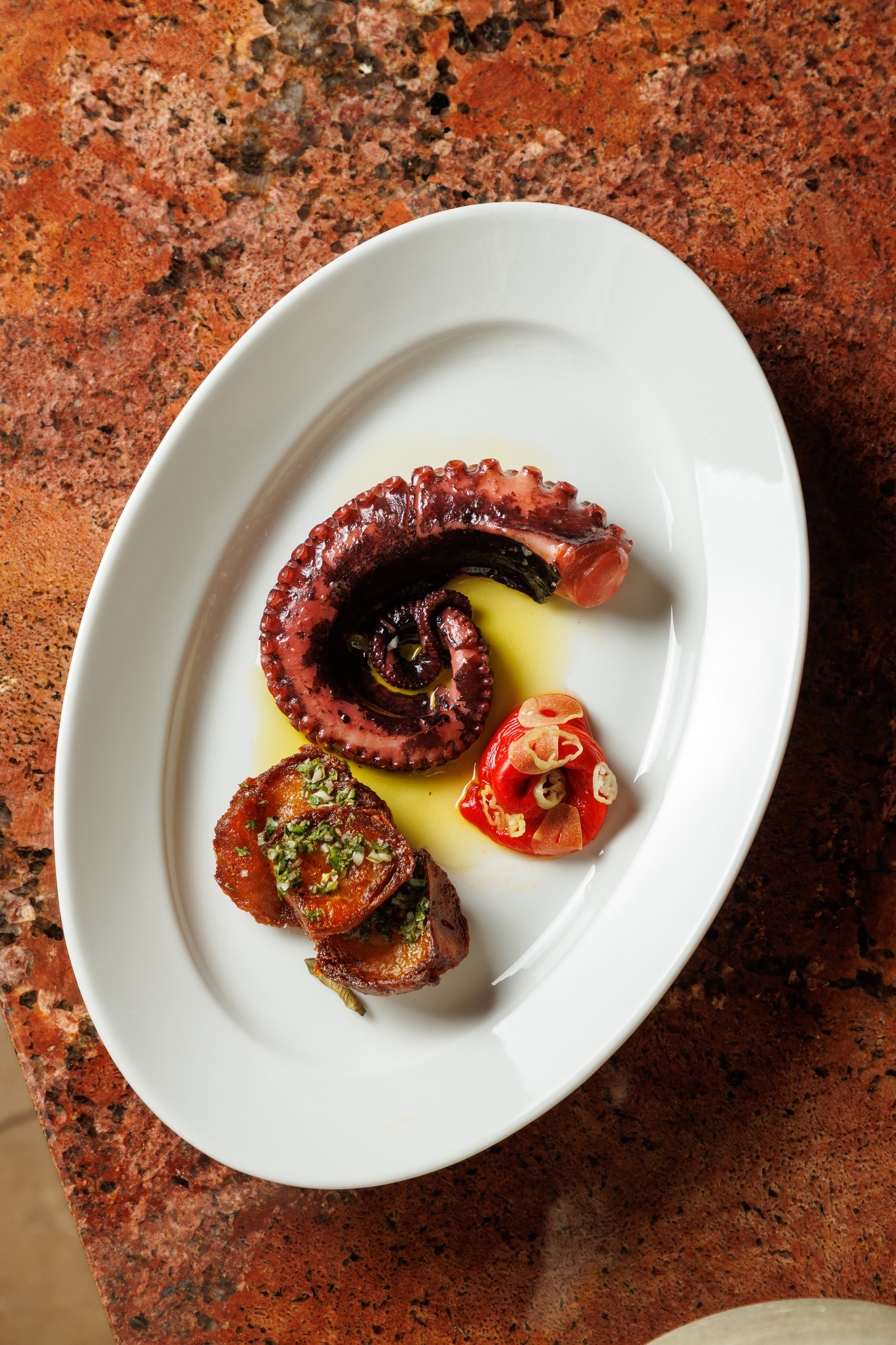 Grilled octopus with potatoes and salsa on a white plate, set on warm marble
