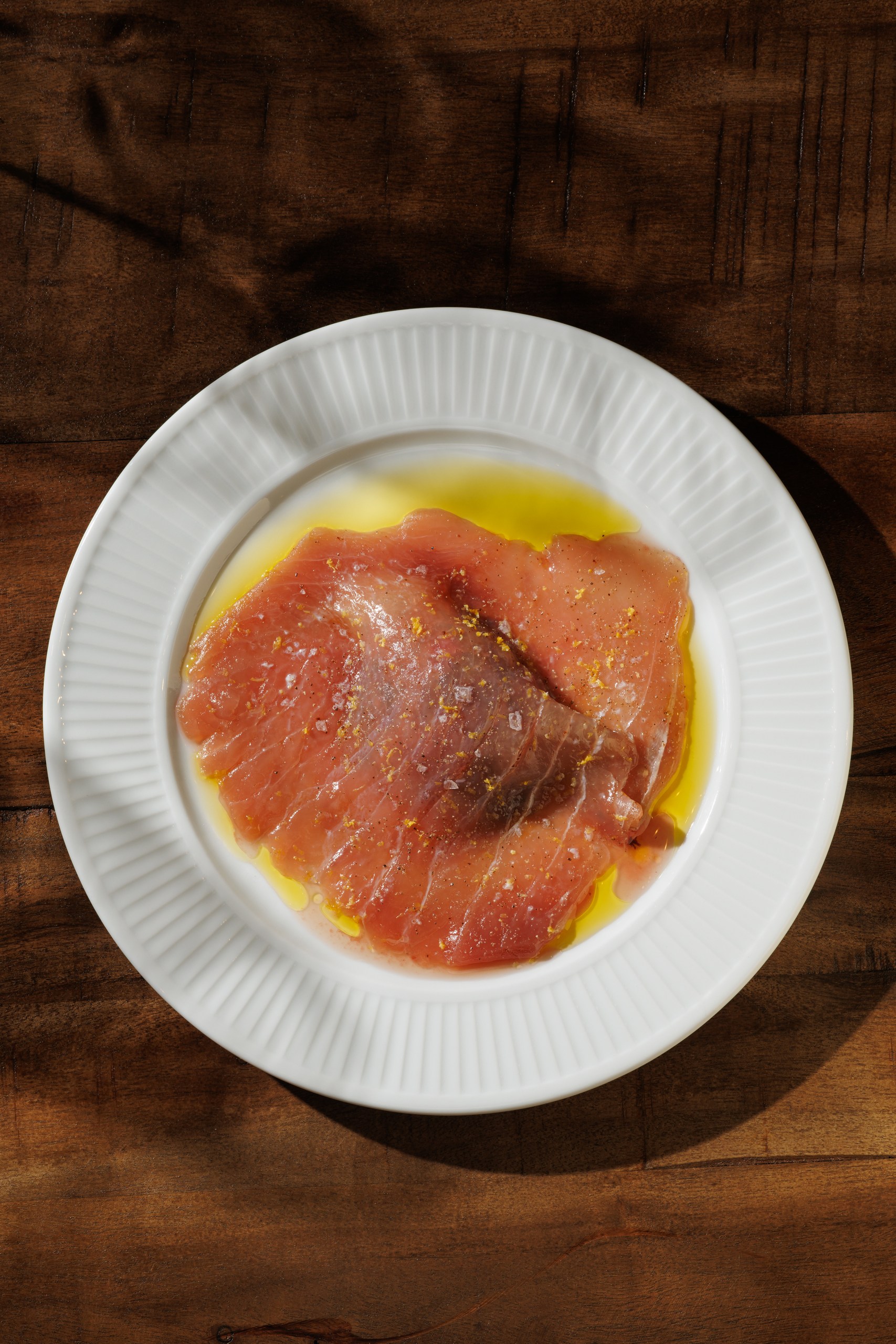 Tuna crudo with citrus zest on a white rimmed plate
